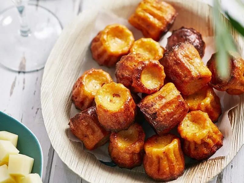 Assiette rustique avec des cannelés salés dorés, quelques morceaux de chorizo et une branche de thym