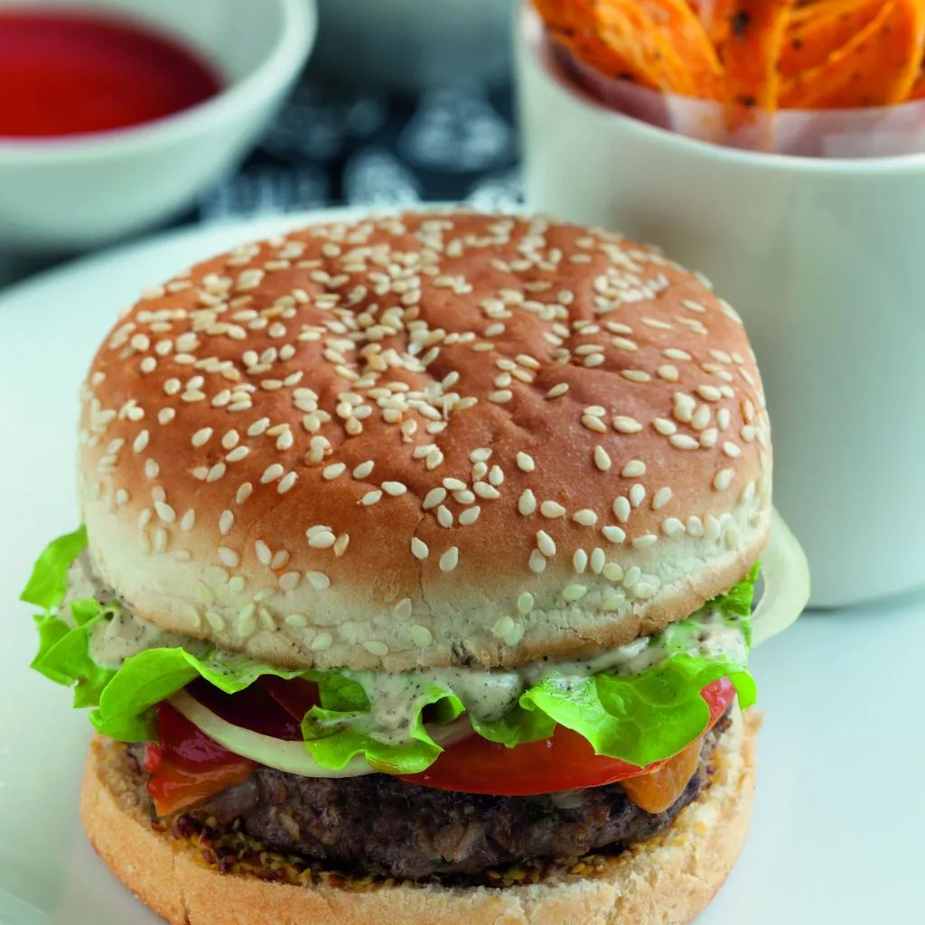 Burger maison posé sur une planche en bois, pain brioché doré, steak juteux, rondelles d'oignon rouge et salade verte à côté